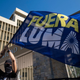 A woman waves a flag that reads in Spanish “LUMA Out” during a protest in front of the headquarters of LUMA Energy, the company that took over the transmission and distribution of the island’s electric authority.